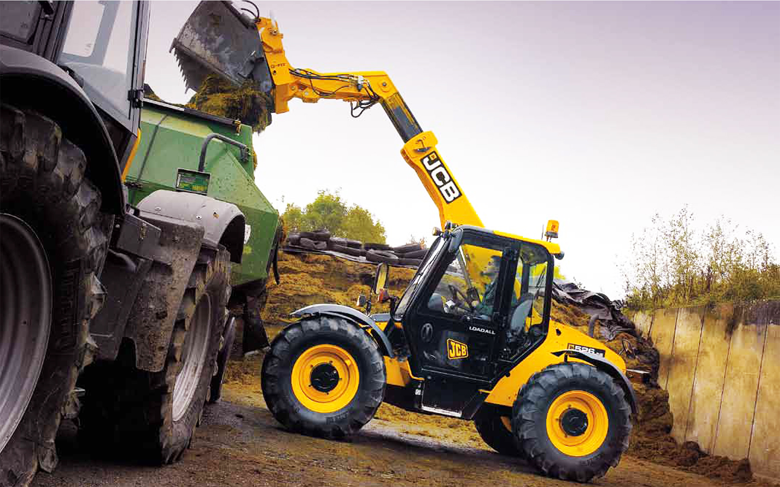 Фото 1. JCB 526-56 Loadall с ковшом-измельчителем слежавшейся силосной массы при загрузке прицепной кормокухни